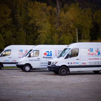 Three white 21 Degrees Hugh's Heating and Air Conditioning vans parked side by side with tall trees in the background